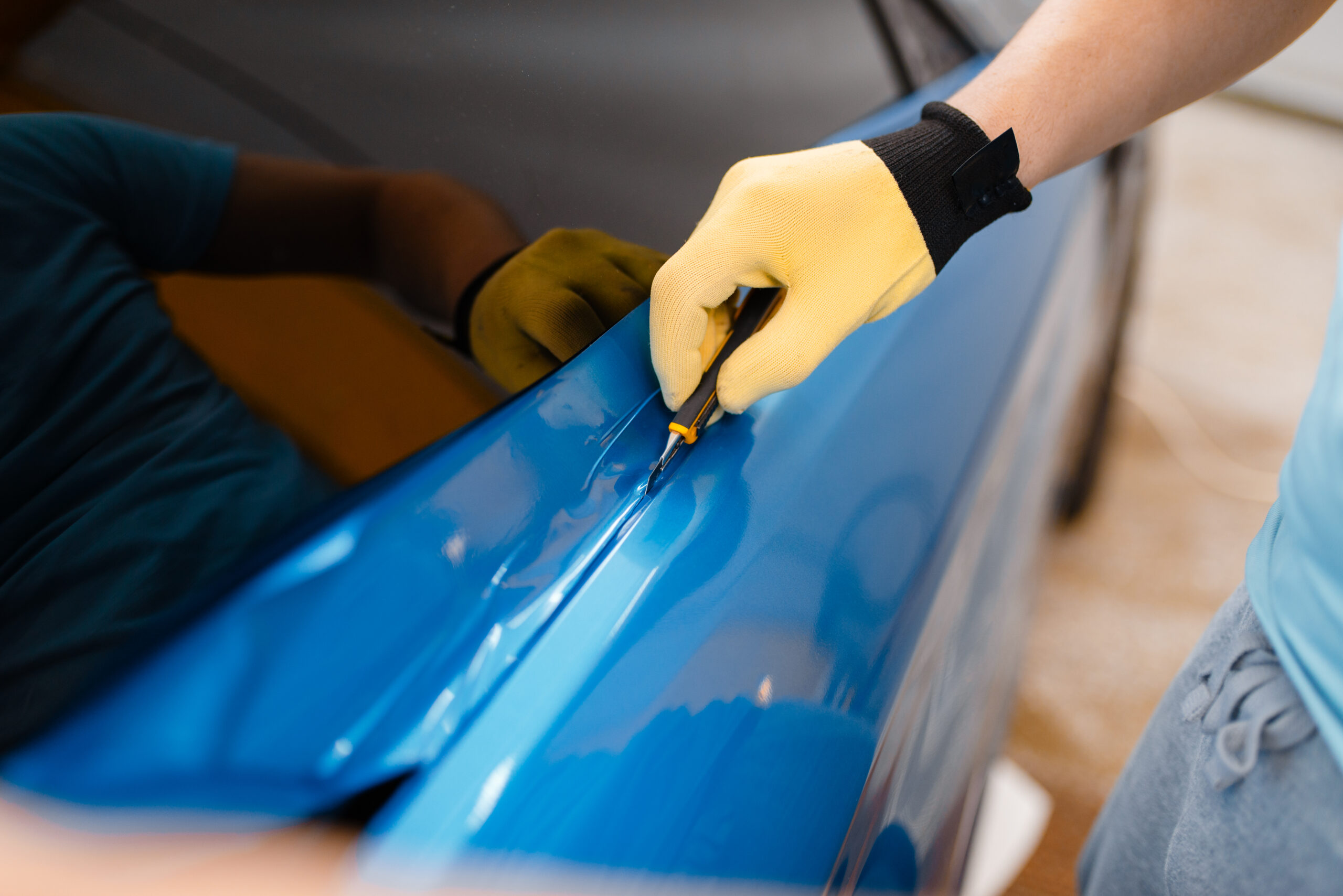 Een specialist brengt een blauwe folie aan op een auto bij Vino Automotive